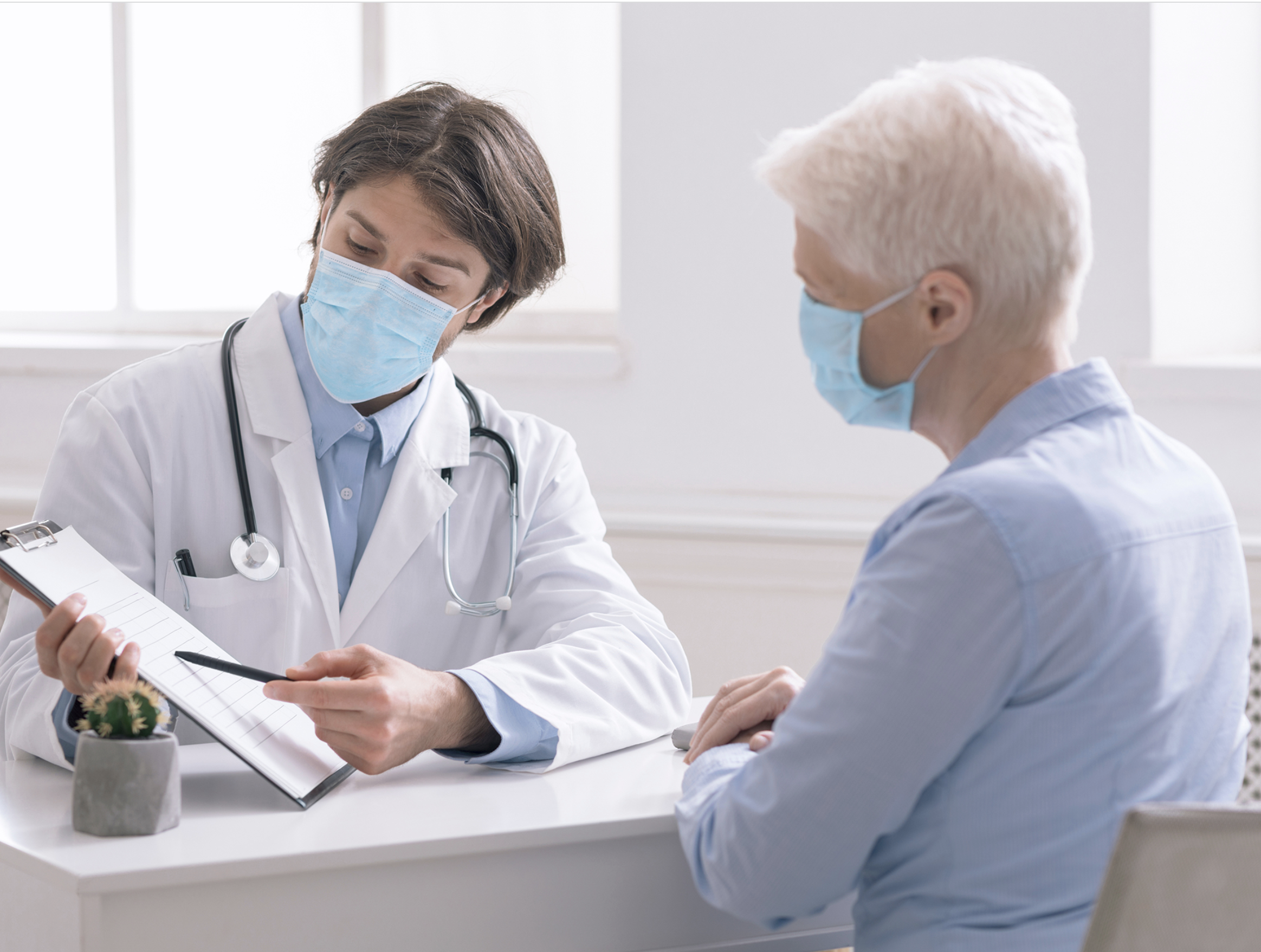 A masked up male doctor is showing medical cost to an older patient likely a COVID hauler patient, medical billing during covid.