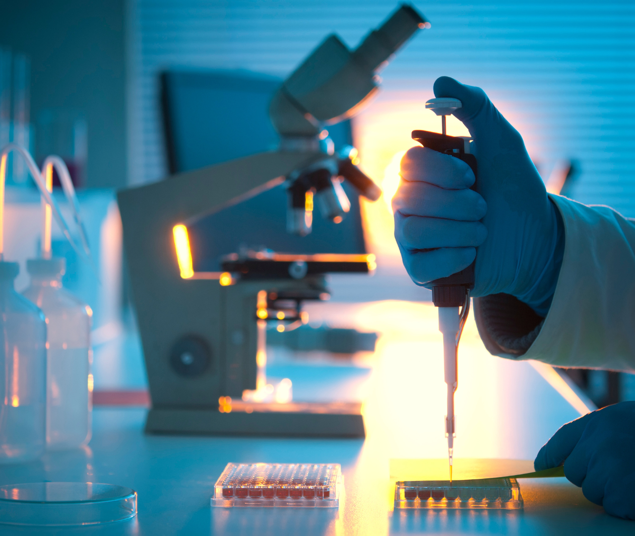 Coronis health lab worker using a pipette near a microscope
